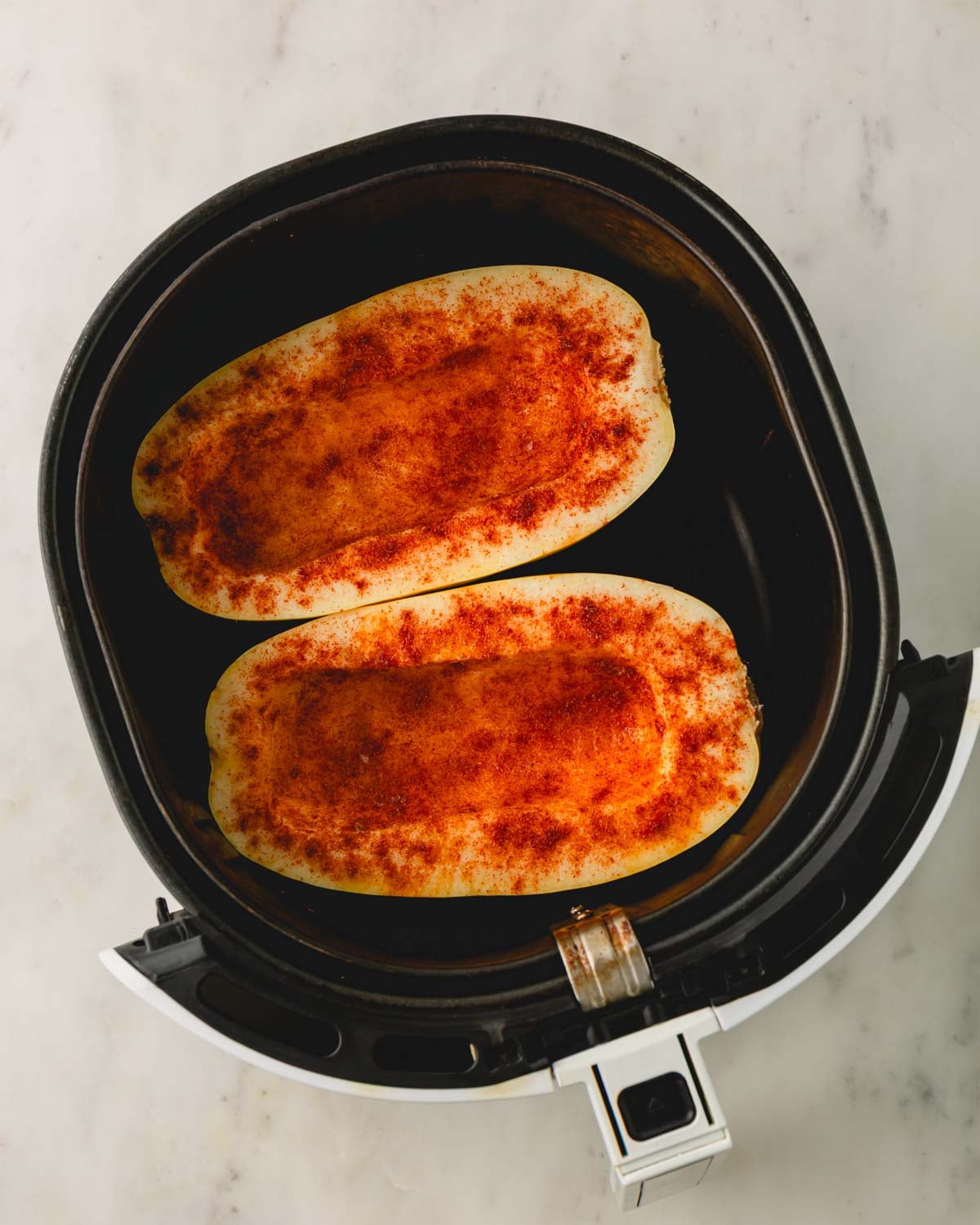 Spaghetti squash halves placed in an air fryer basket.