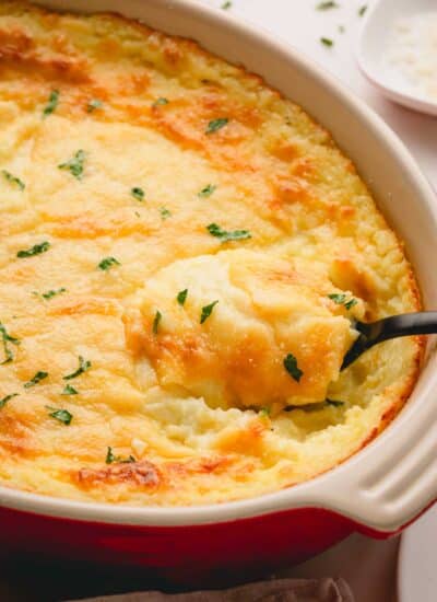 Cheesy mashed potatoes in a baking dish with a black spoon scooping some out.