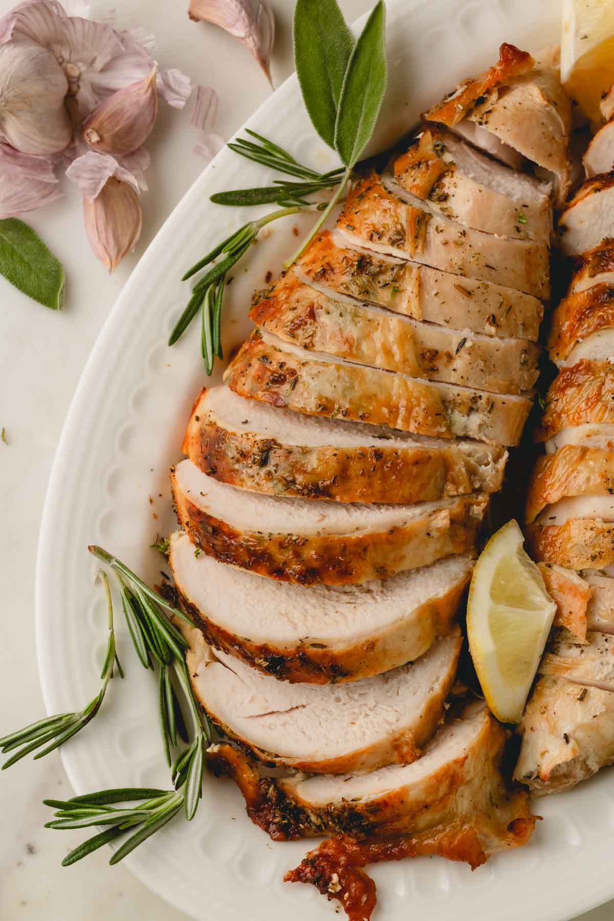 Sliced turkey breast on a white platter with rosemary and lemon.