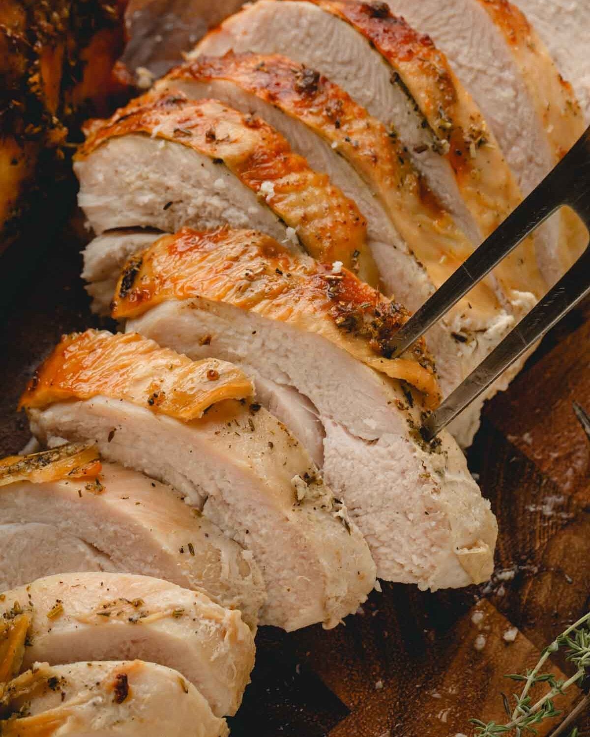 Closeup image of sliced turkey breast on a cutting board with a meat fork sticking into one slice.