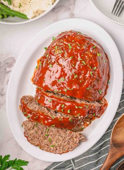 One pound meatloaf with slices cut on a white platter with mashed potatoes in the background.