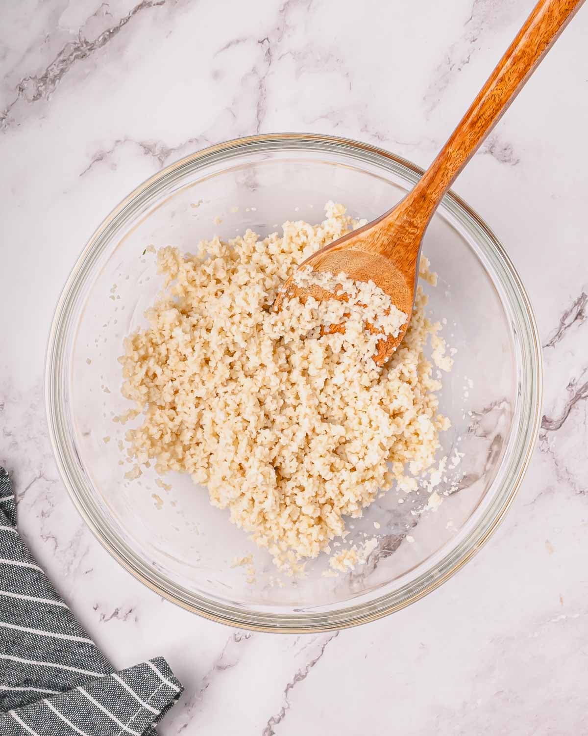 A glass bowl with breadcrumbs soaking in milk with a wooden spoon resting in the bowl.