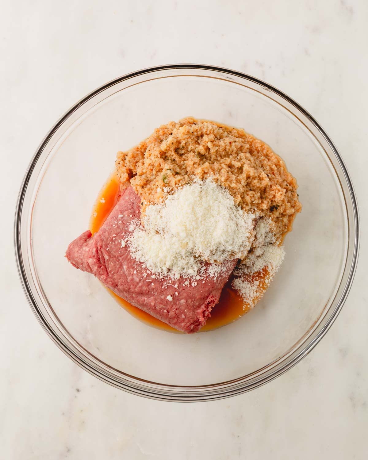 A glass bowl with the ground beef, parmesan cheese, and panko breadcrumbs.