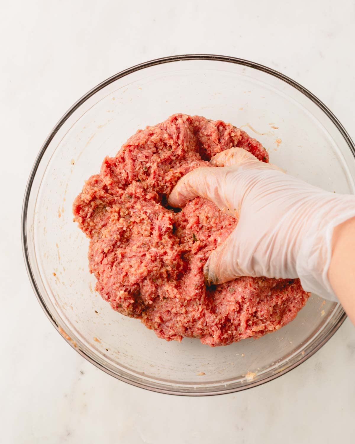 A hand with a glove mixing the air fryer meatloaf mixture in a glass bowl.
