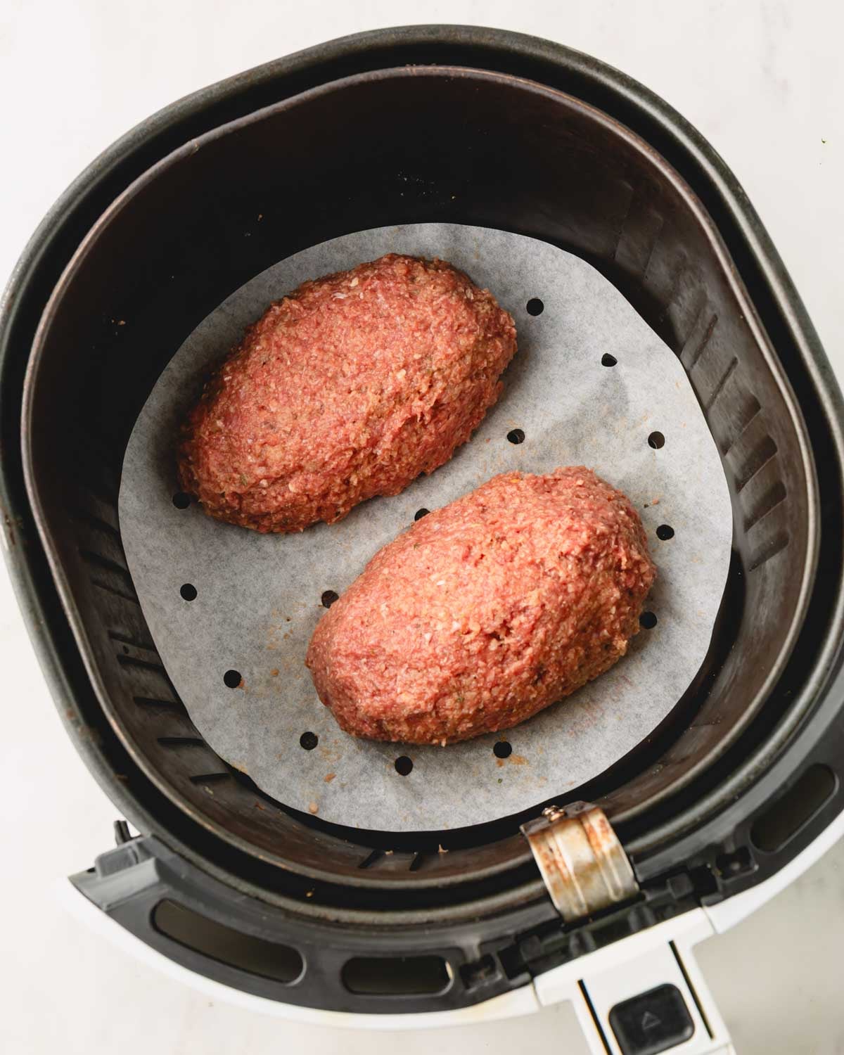 Two shaped meatloaves on a piece of parchment paper in the air fryer.