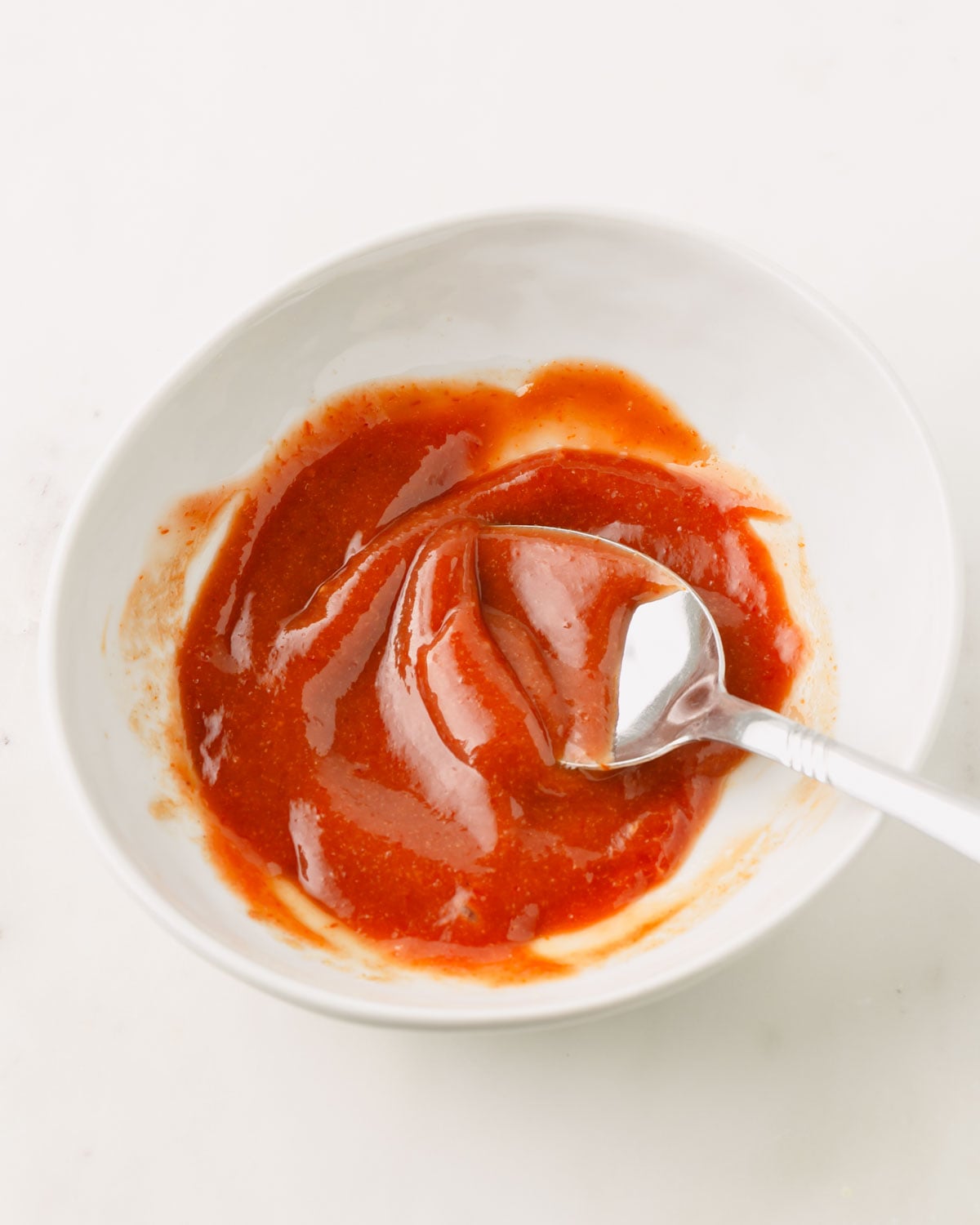 A white bowl with a spoon with the ketchup glaze for the meatloaves.