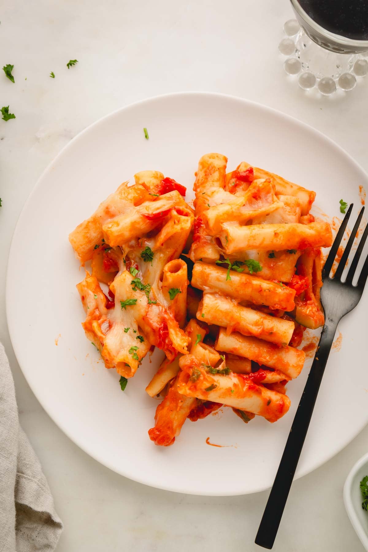 A white plate with baked vegetarian ziti and a black fork.