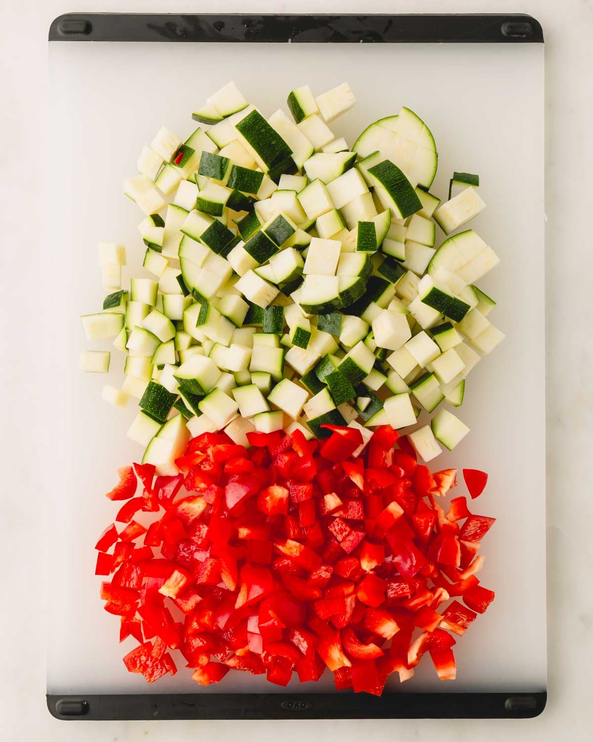 Chopped zucchini and red bell pepper on a plastic cutting board.