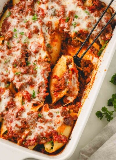 Beef and ricotta stuffed shells in a white casserole dish with a black serving spoon.