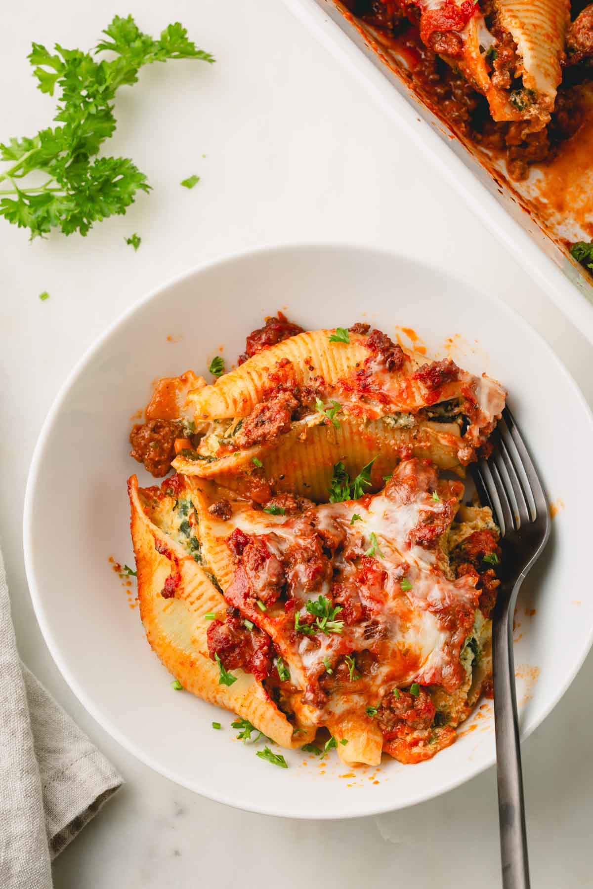 A white bowl with beef and ricotta stuffed shells with a fork.