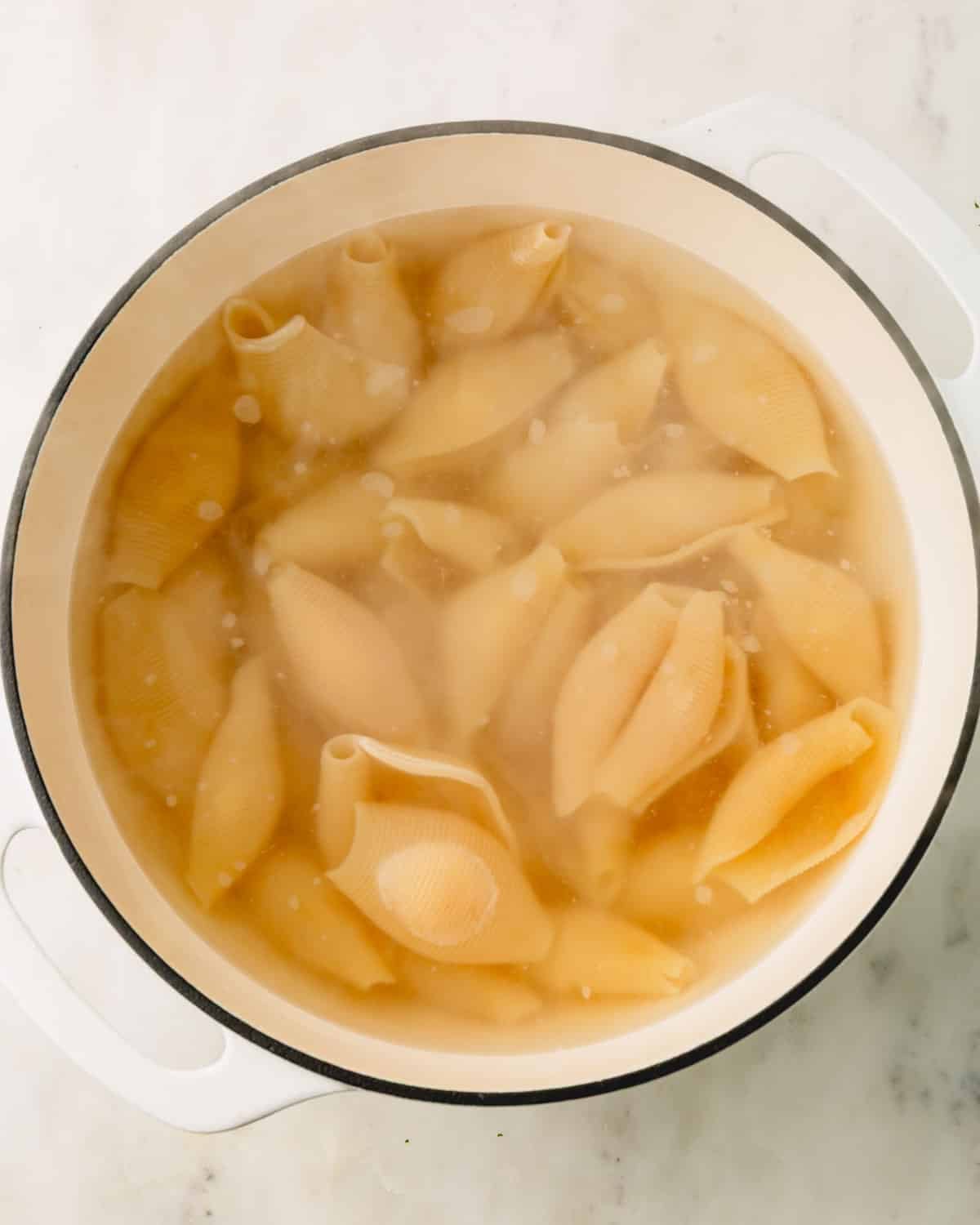 A white pot with jumbo pasta shells boiling.