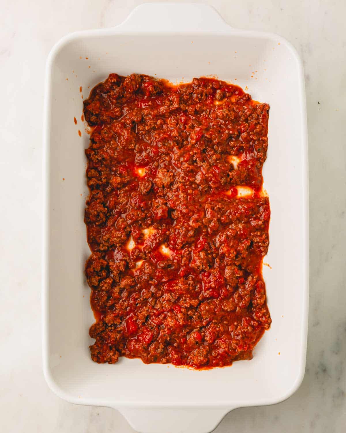 A white casserole dish with the meat sauce in the bottom.