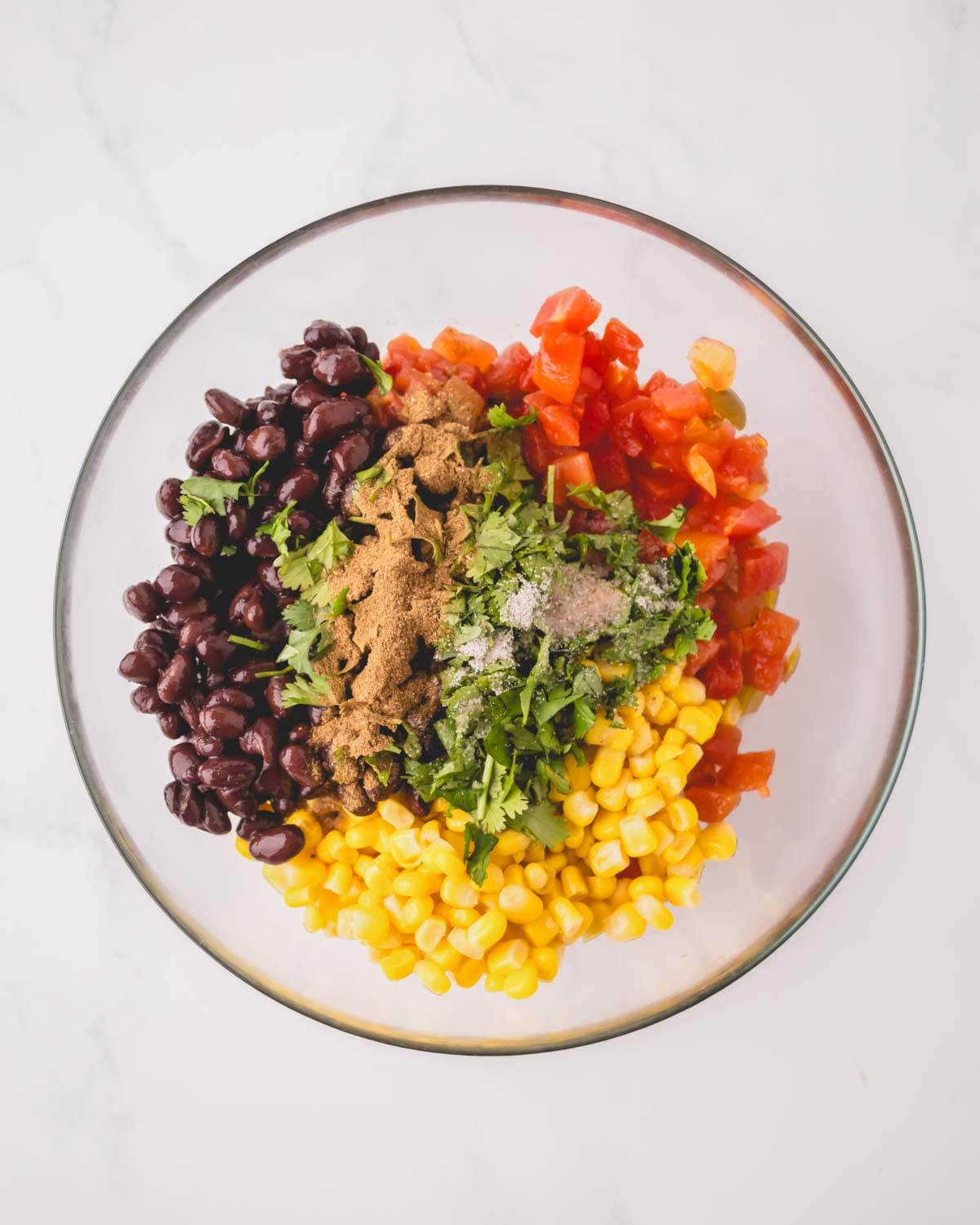 A glass bowl with ingredients for corn and black bean salsa.
