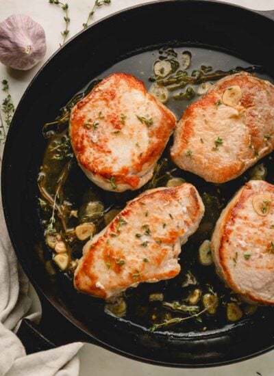 Pan seared pork chops in a cast iron pan with garlic and herbs.