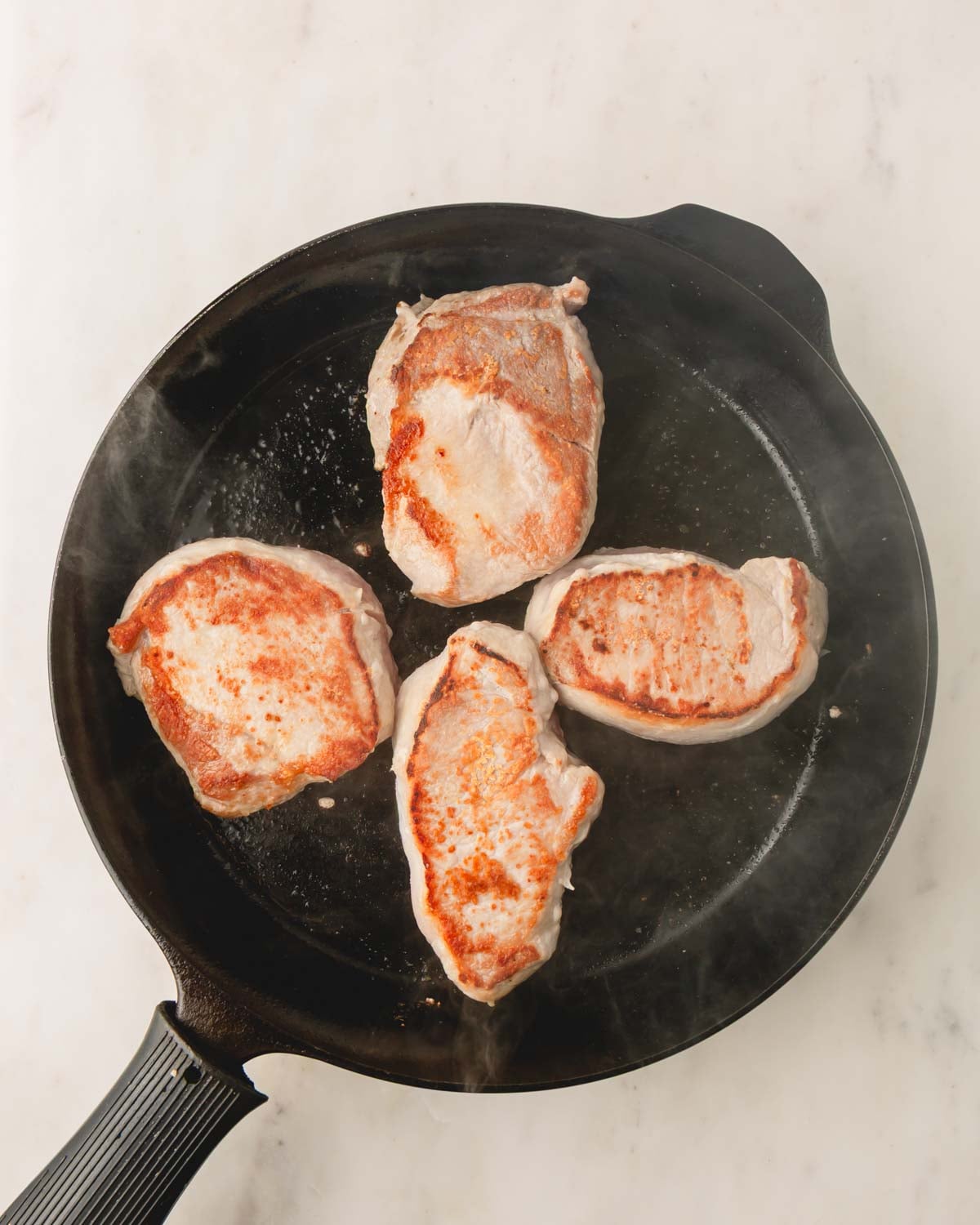 A cast iron skillet is browning 4 pork chops.