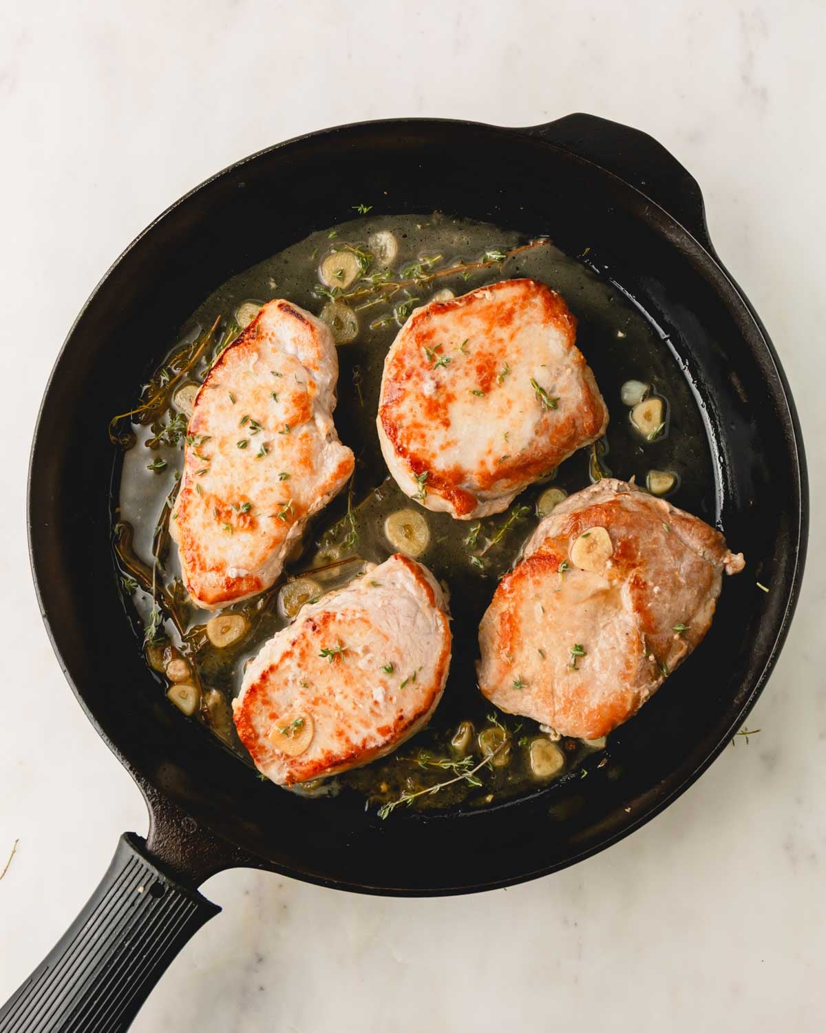 A cast iron skillet with 4 pan seared pork chops and a garlic wine sauce.