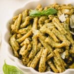 Creamy pesto pasta in a white bowl with basil on top.