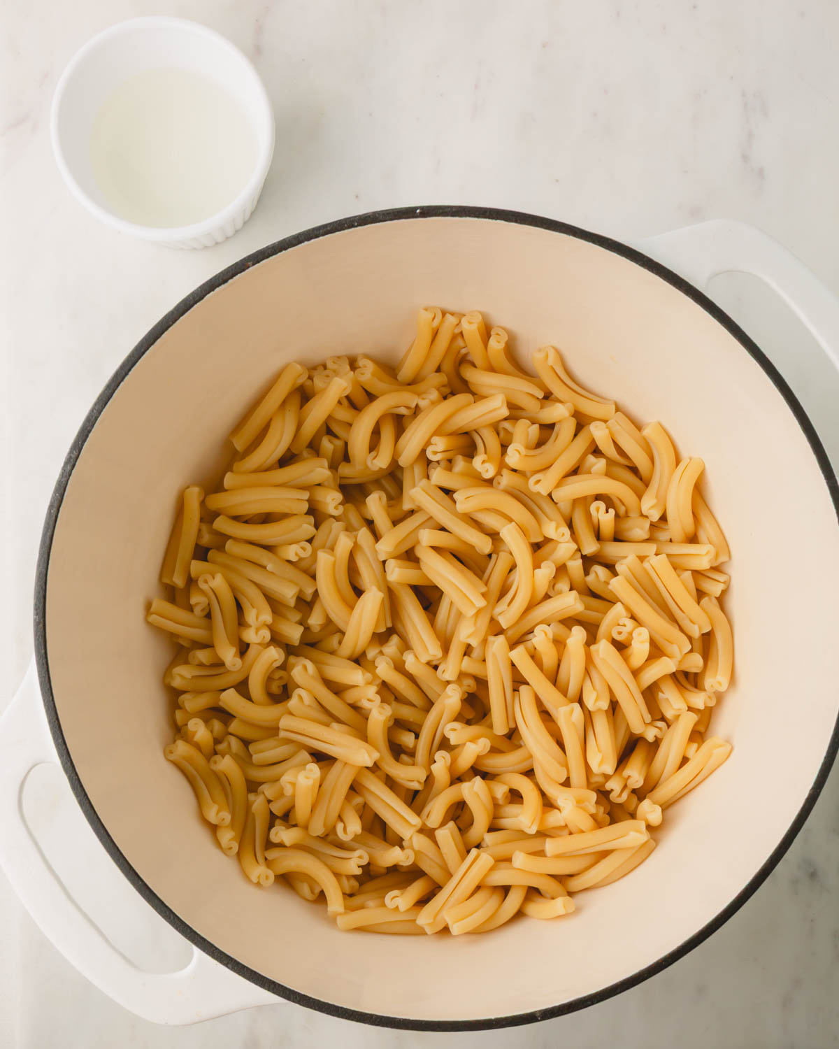 Boiled noodles in a large white pot with some of the reserved pasta water.