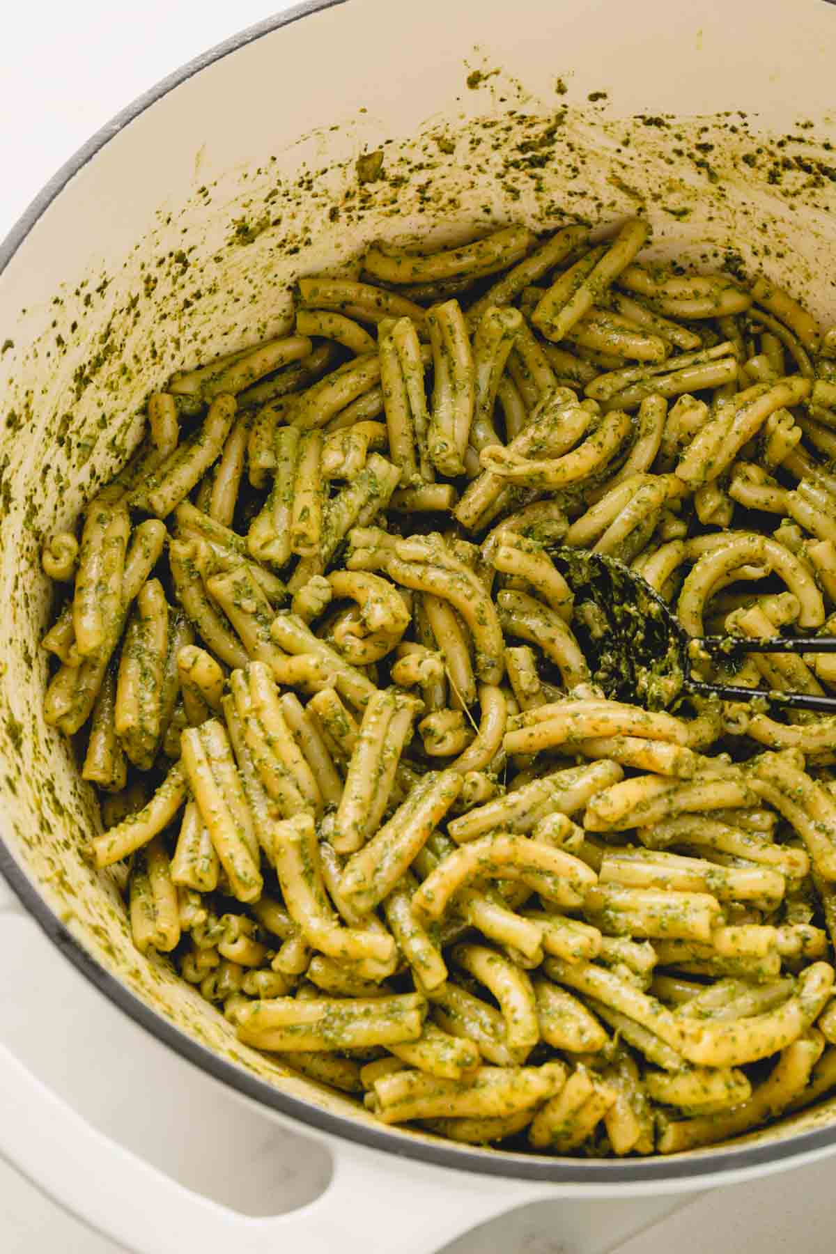 Creamy pesto pasta in a large white pot with a black spoon in the noodles.