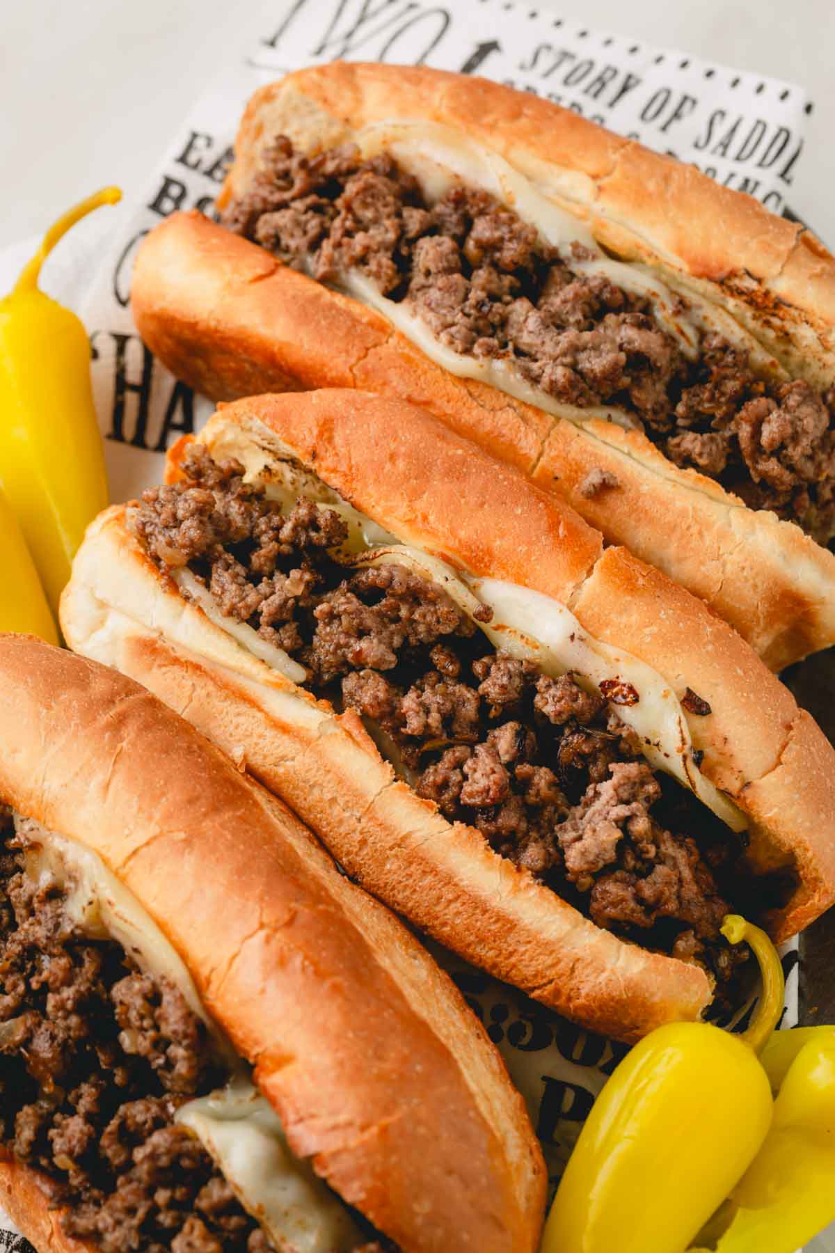 Three ground beef cheesesteaks with banana peppers on the side.