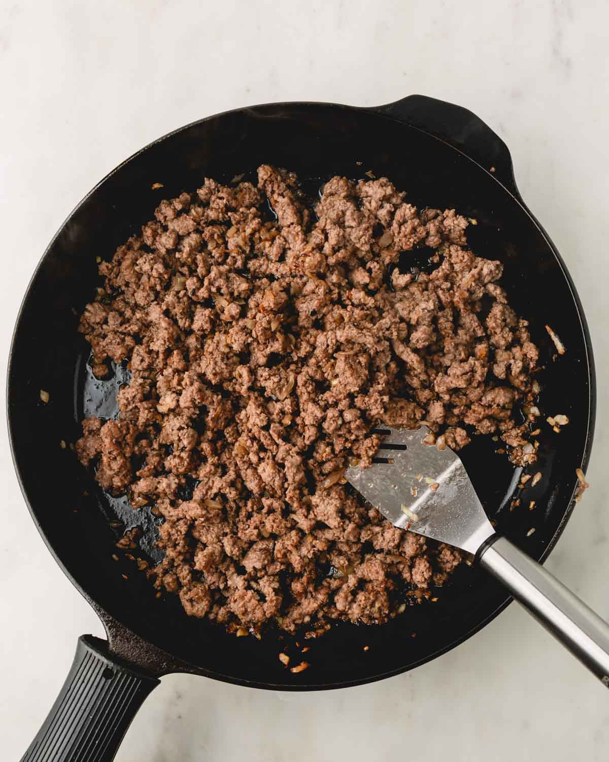Ground beef in a skillet with a stainless steel spatula.