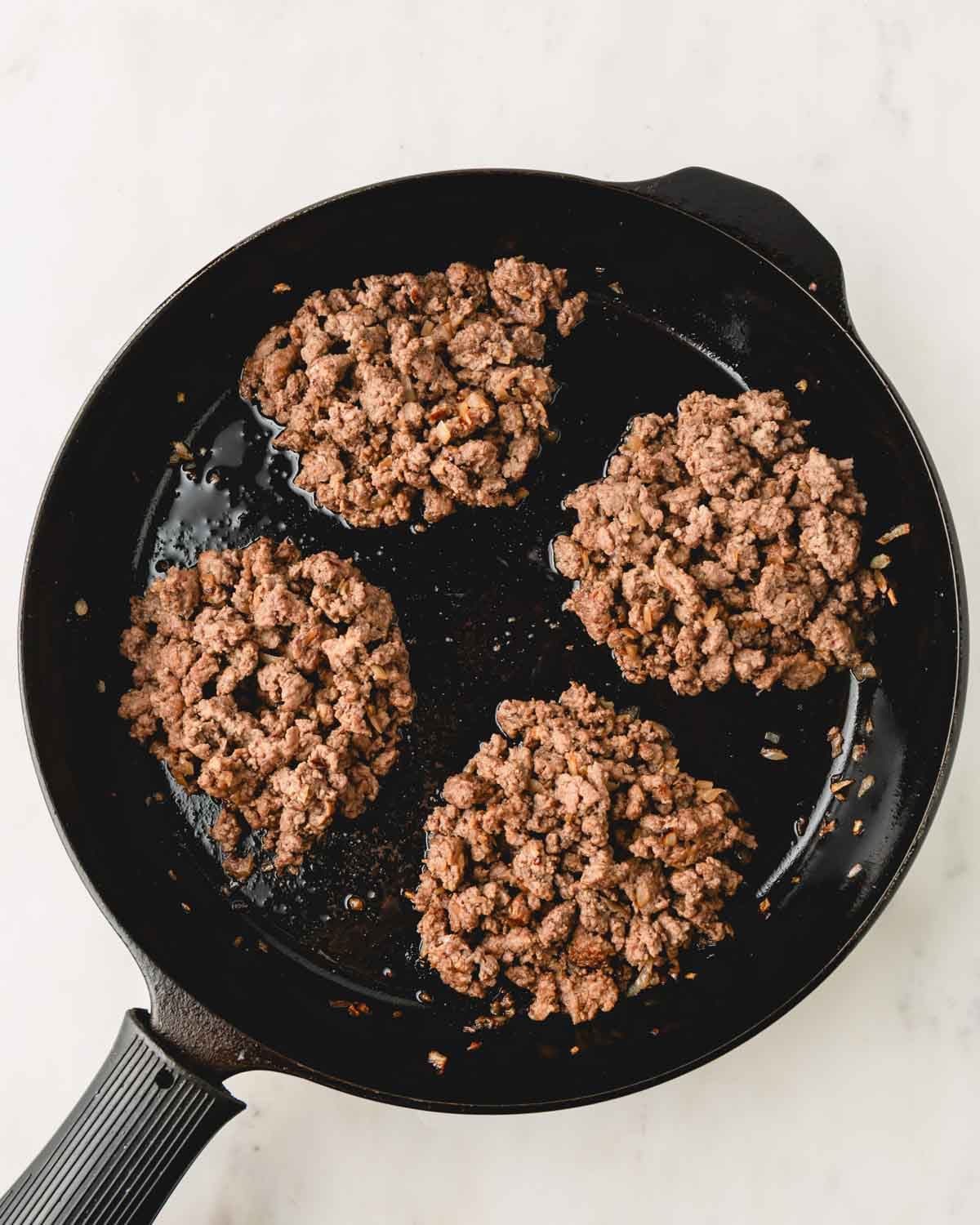 Four piles of ground beef in a skillet.