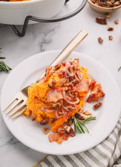 Savory sweet potato casserole on a white plate with a gold fork.