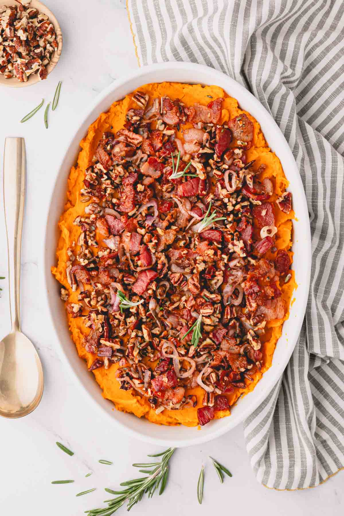 Baked savory sweet potato casserole with a striped linen and gold spoon.