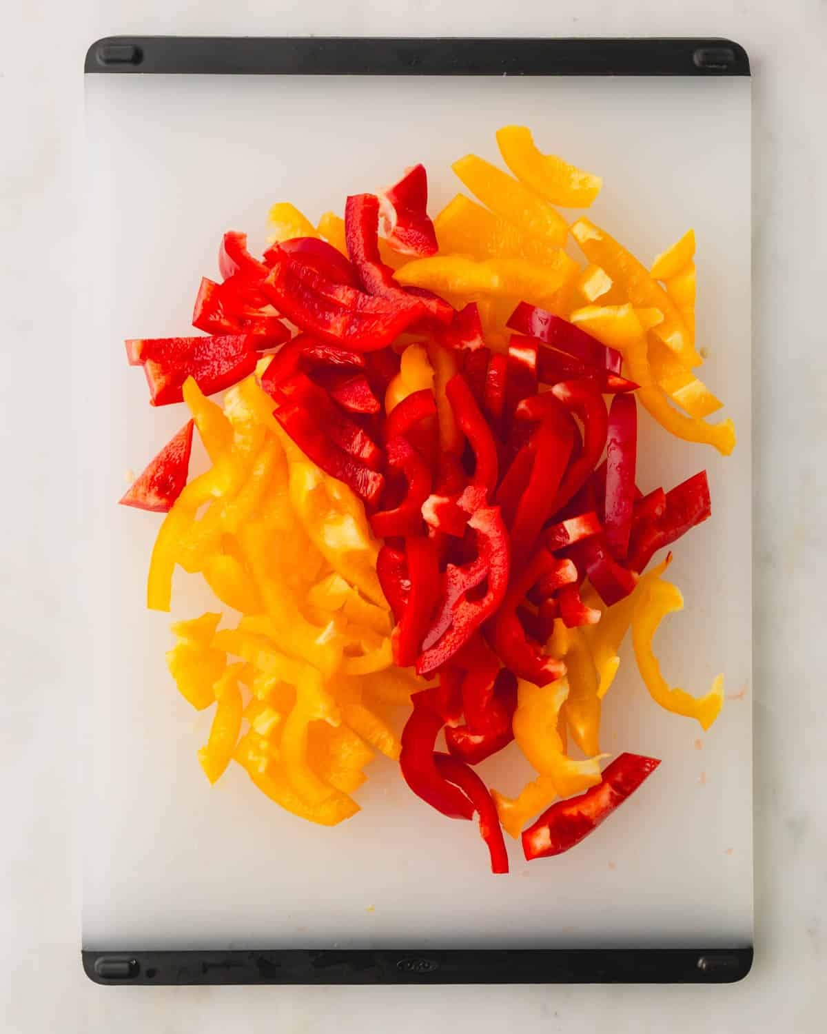 A plastic cutting board with red and yellow bell pepper slices.
