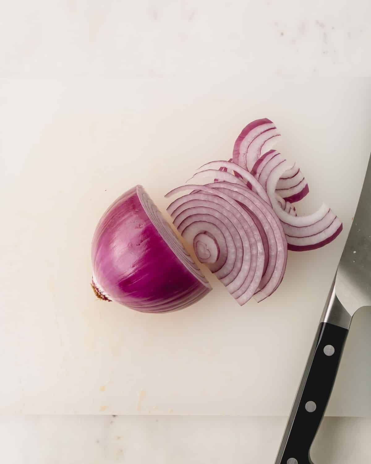 A red onion is being sliced on a cutting board with a chef's knife.