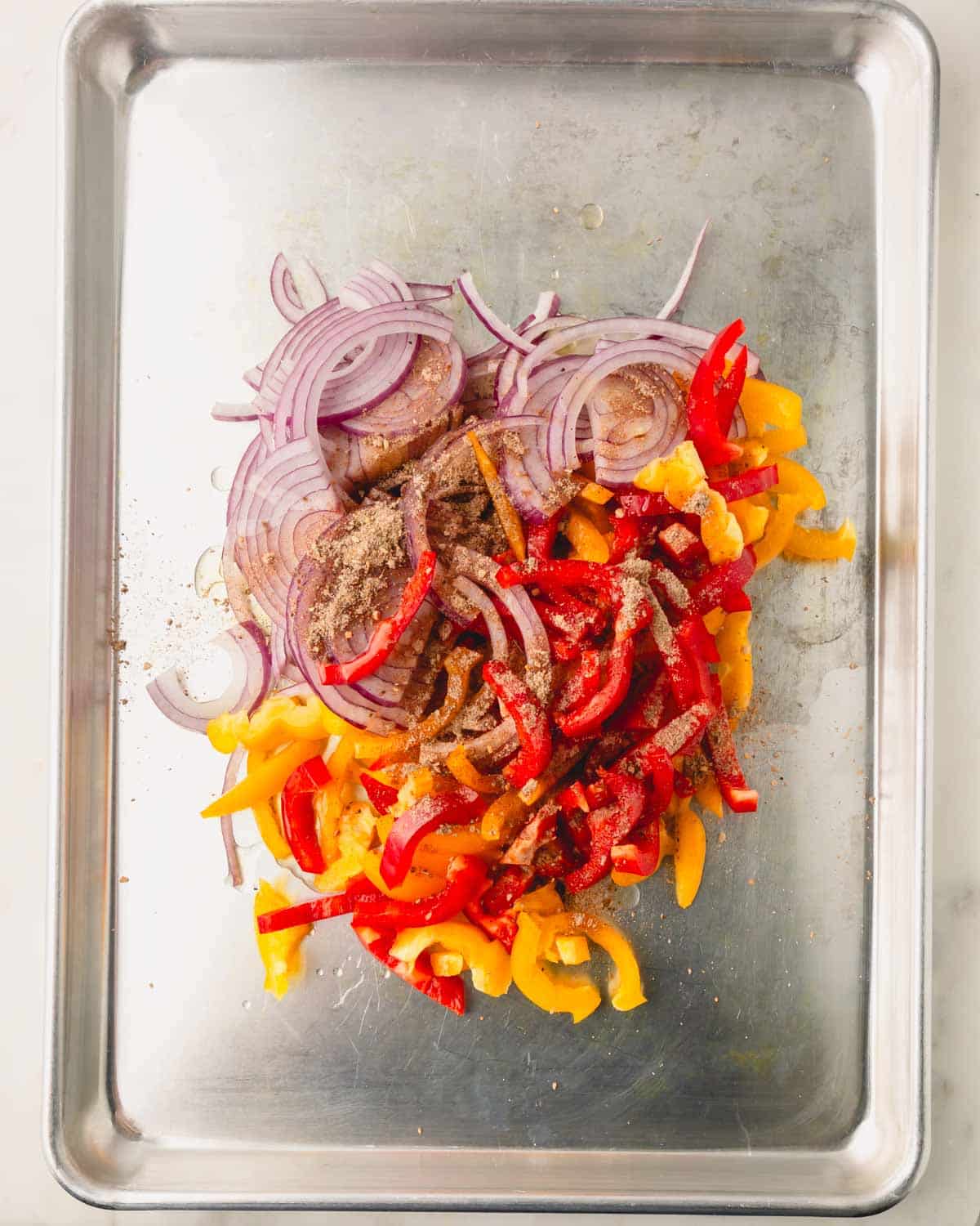 A sheet pan with sliced onions and bell pepper with fajitas spices.