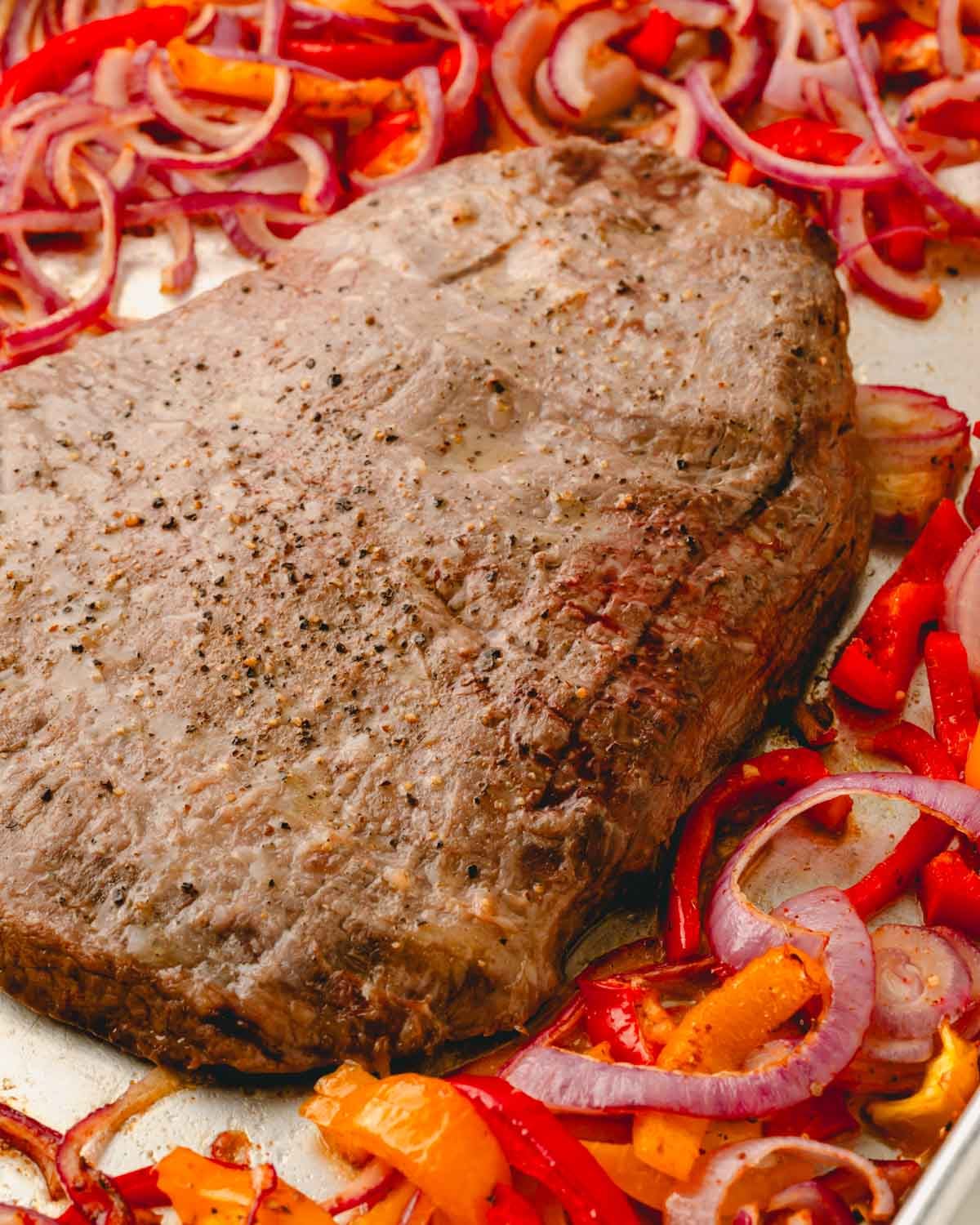 Close up of cooked flank steak on a sheet pan with roasted vegetables.