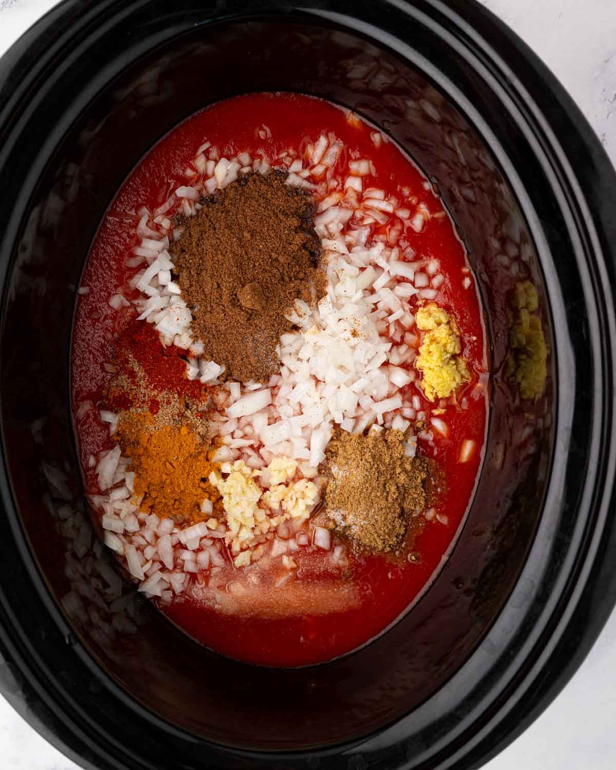 Ingredients for butter chicken sauce in the bowl of a slow cooker.