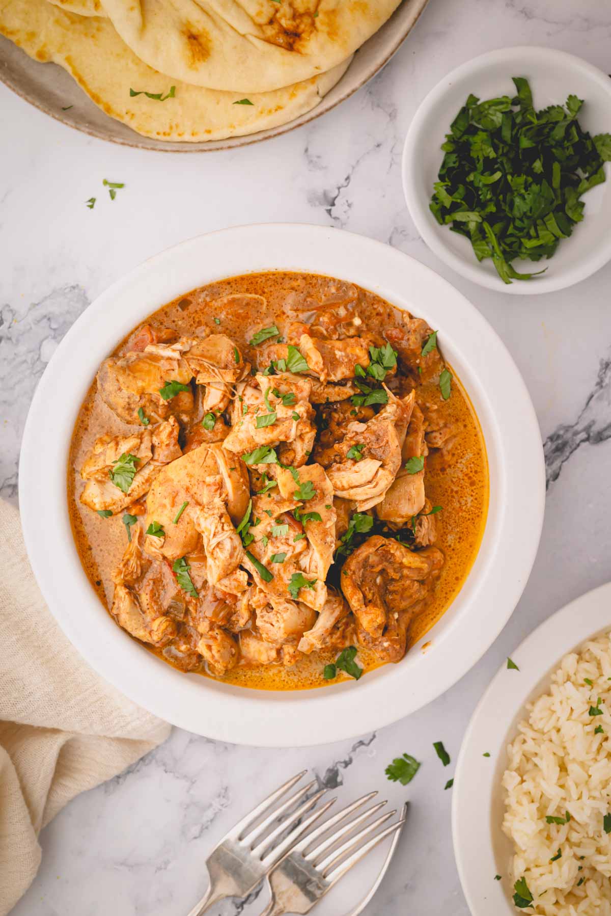 A white plate with slow cooker butter chicken with naan and rice on plates on the side.