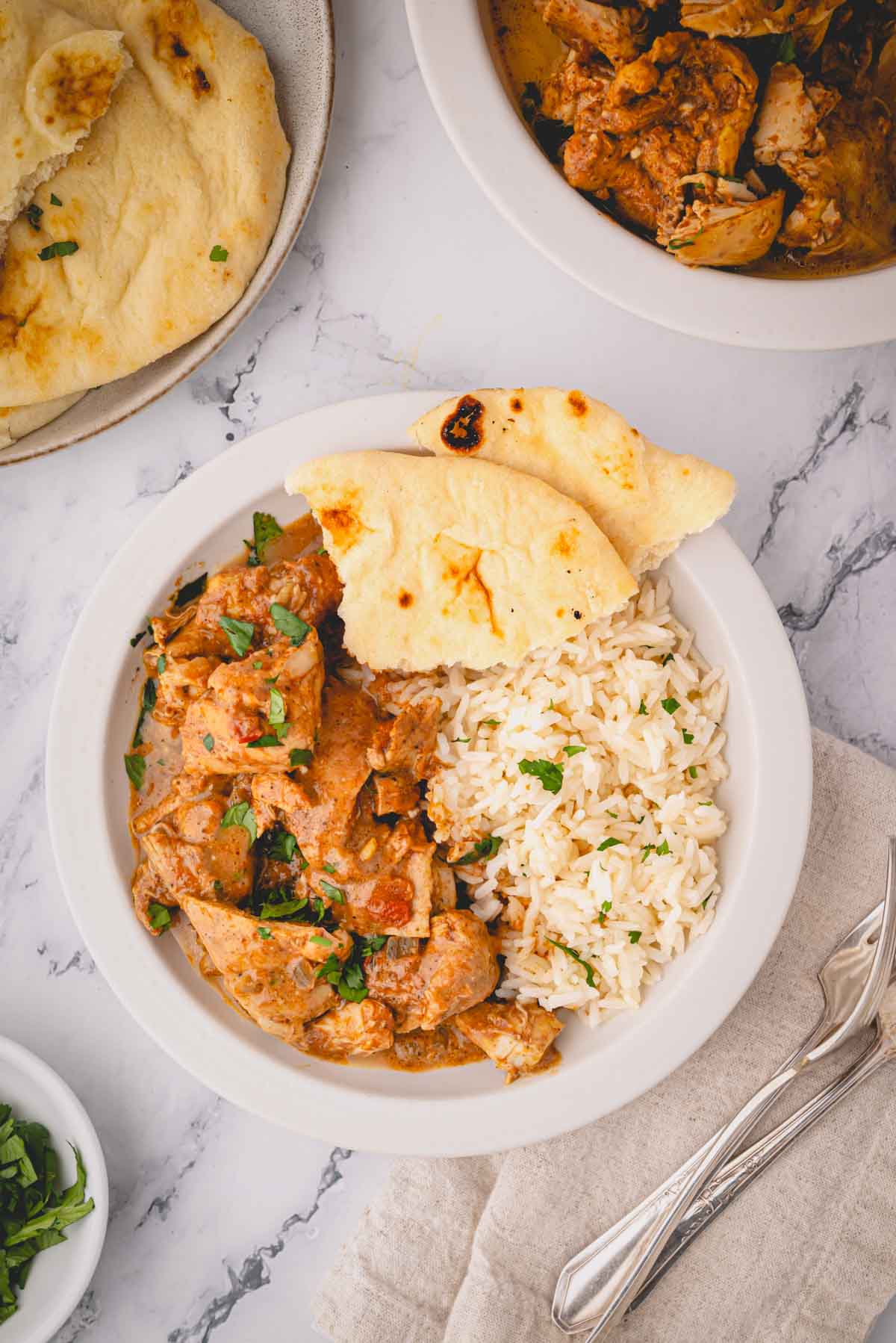 A plate of slow cooker butter chicken with naan and rice on plates on the side.