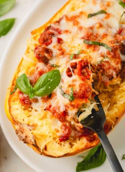 Closeup image of spaghetti squash with meat sauce on a white plate. A black fork is taking a scoop out.