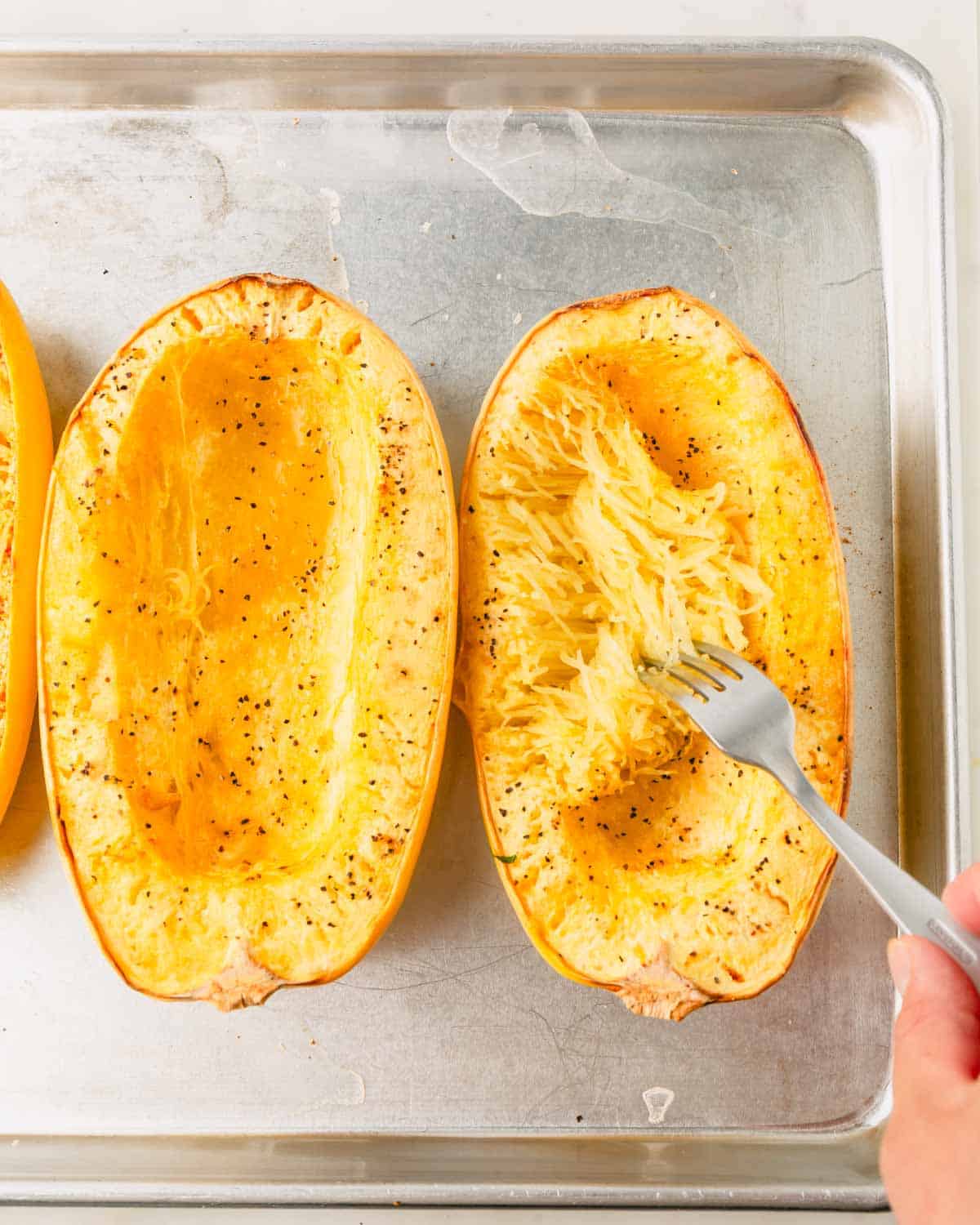 A fork is fluffing the baked spaghetti squash "noodles" on the baking sheet.