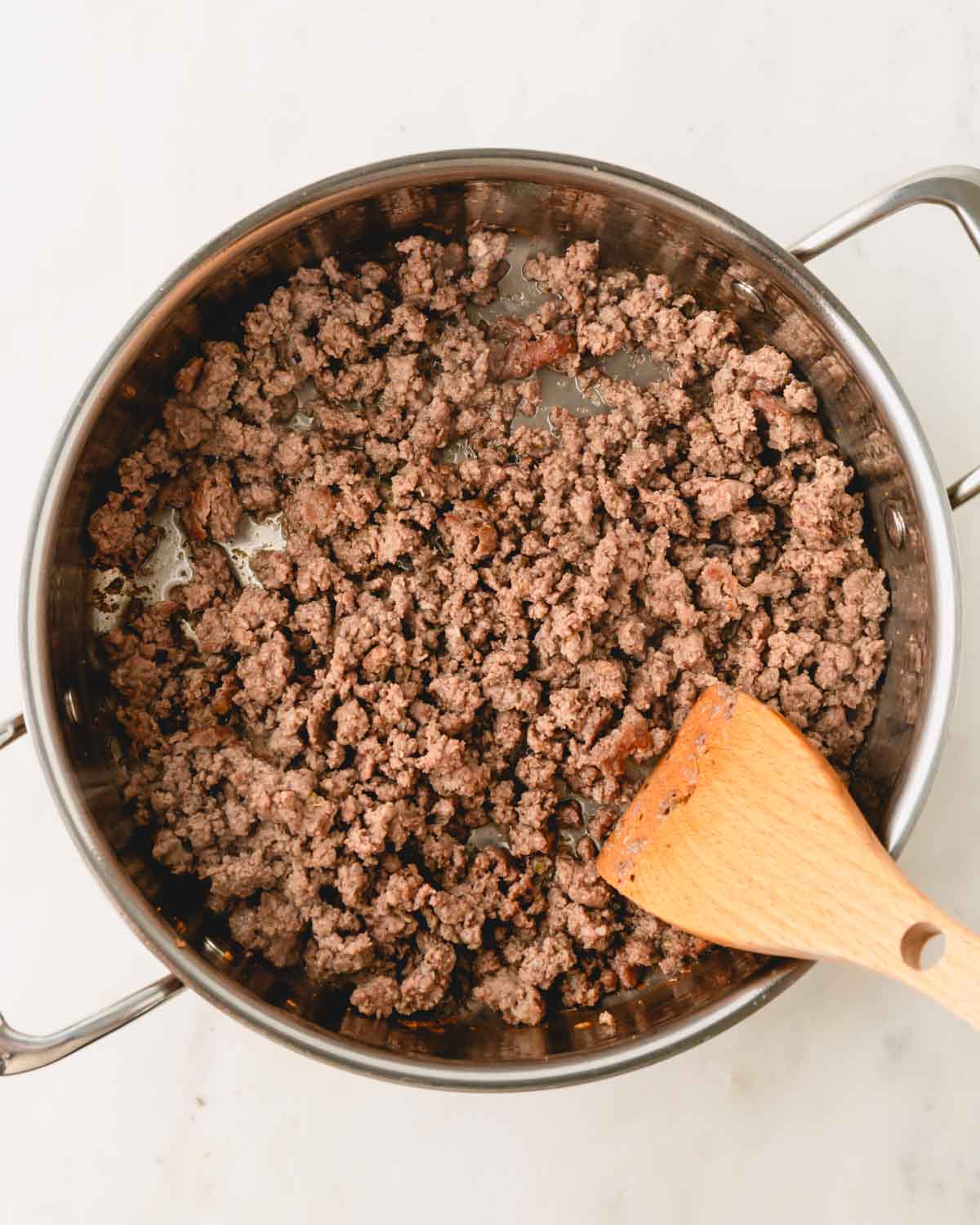 A skillet with browned ground beef and a wooden spatula.