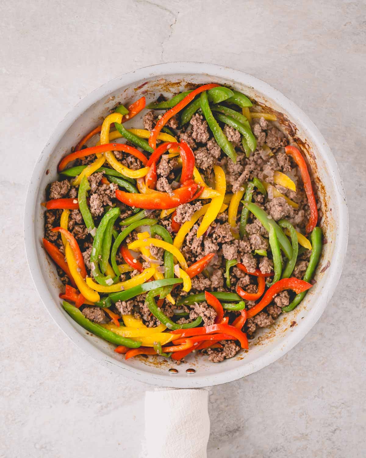 A large skillet with ground beef and peppers cooking.