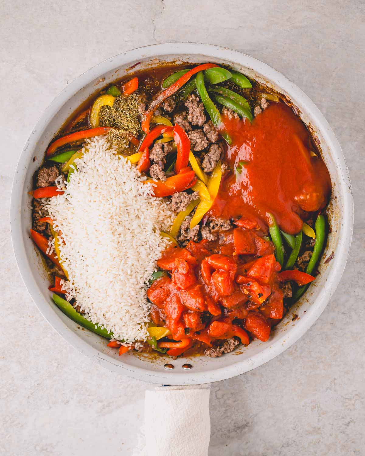 A large white skillet with ground beef, peppers, rice, and tomato sauce.