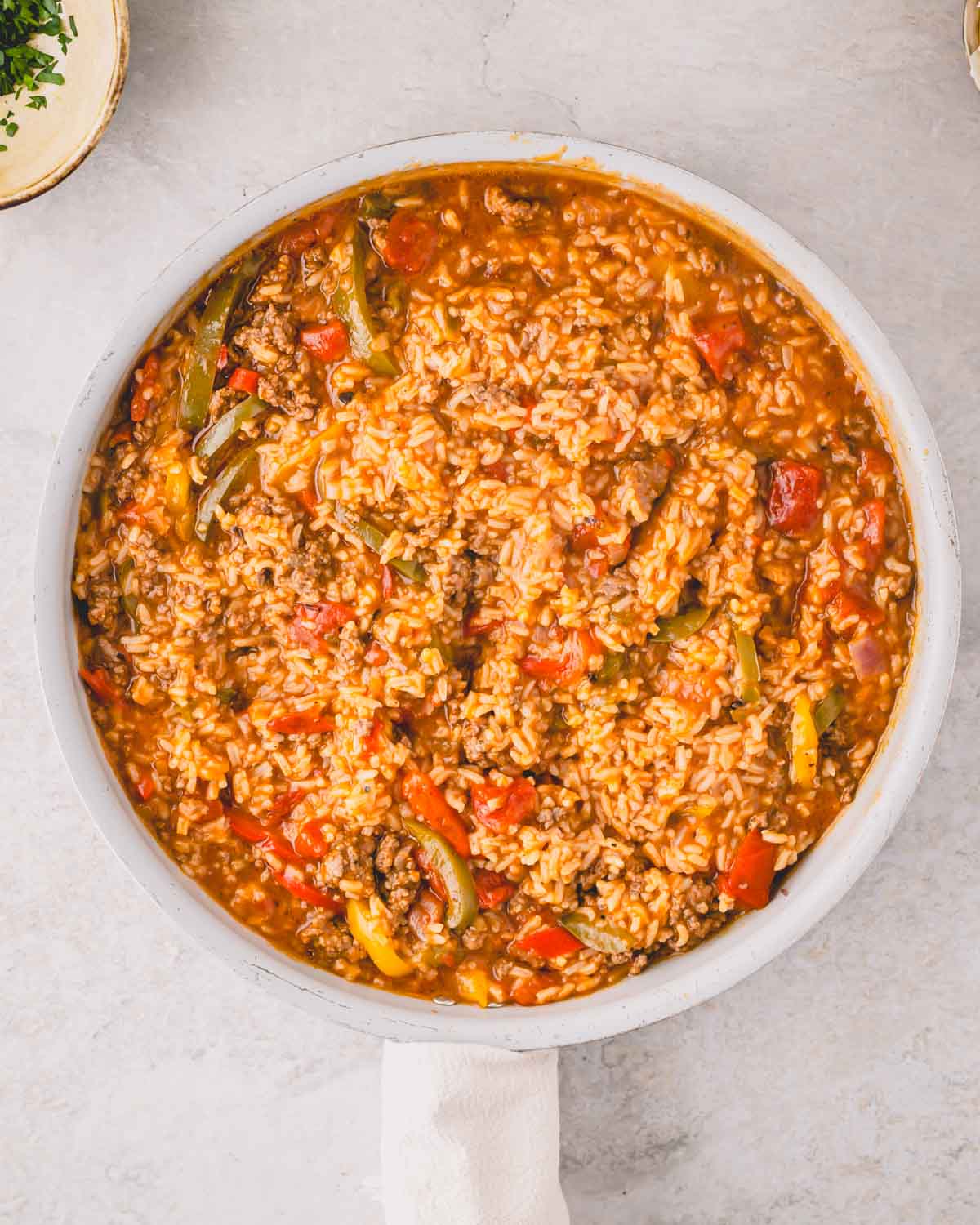 A large white skillet with cooked peppers, rice, beef, and onions.