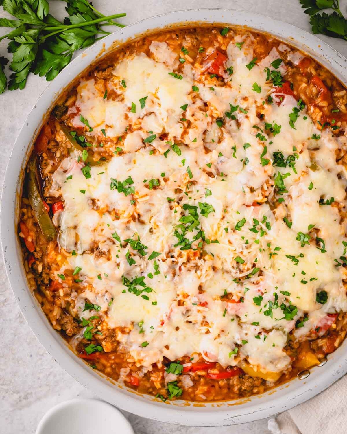 A large white skillet with ground beef, peppers, onions, and melted cheese on top.