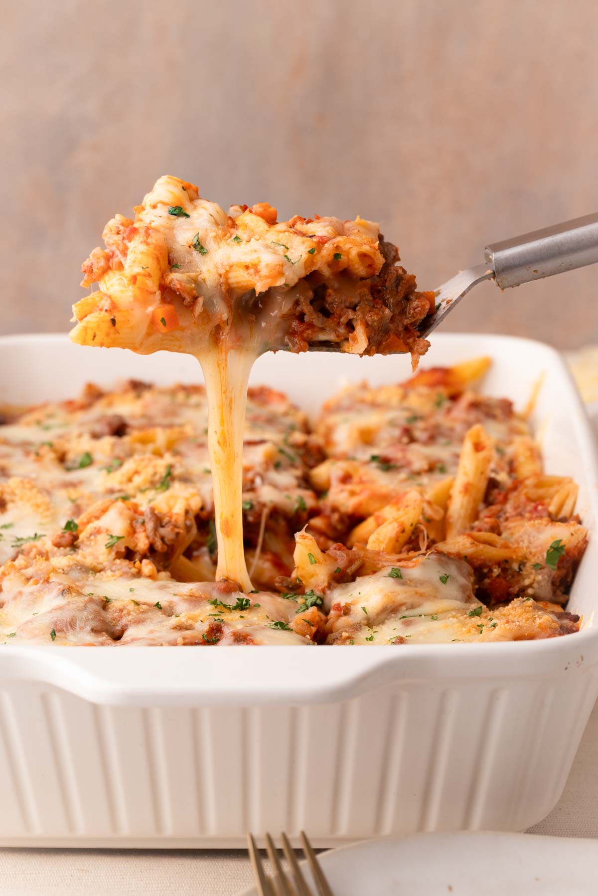 A stainless steel spatula lifting out a scoop of baked pasta bolognese with a nice cheese pull.