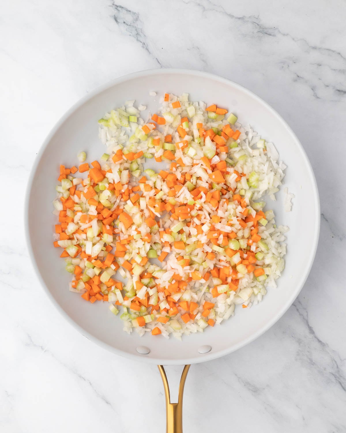 A white skillet with carrots, onion, and celery cooking.
