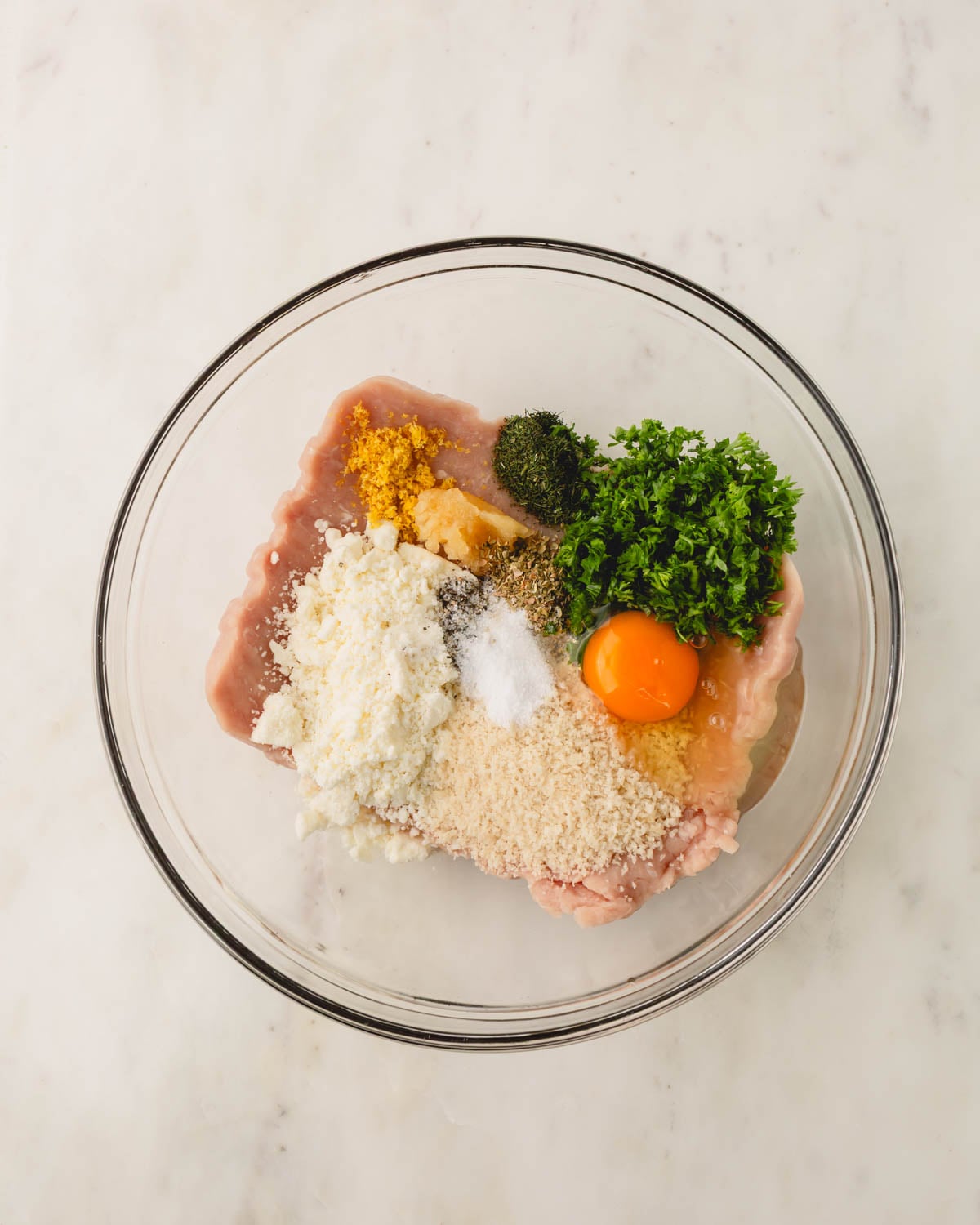 A glass bowl with ingredients for Greek chicken meatballs.