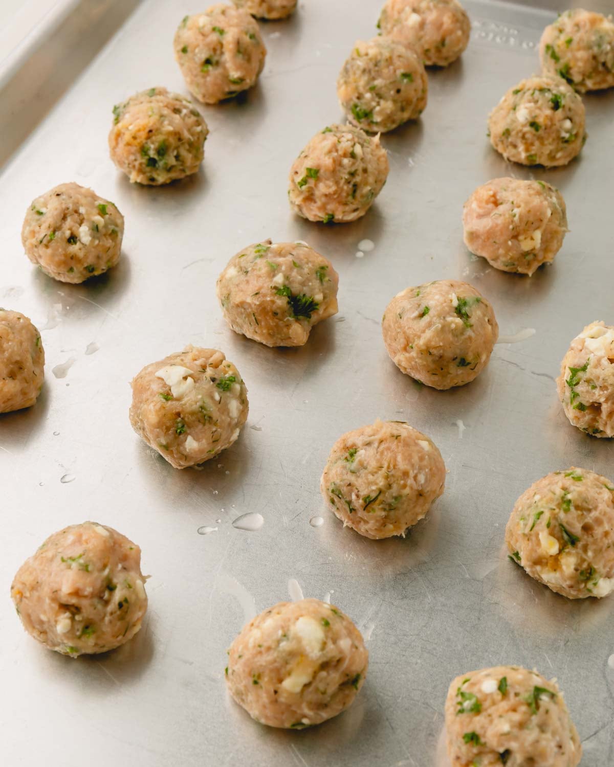 Raw Greek chicken meatballs on a baking sheet.