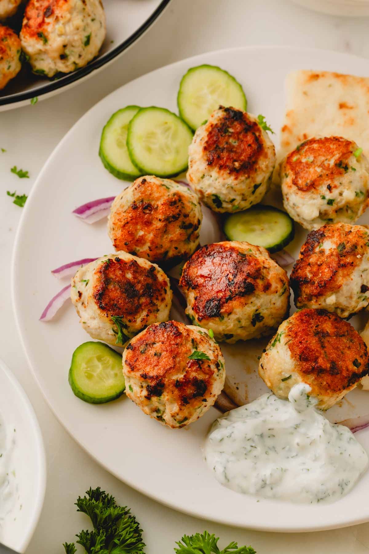 A white plate with Greek chicken meatballs, cucumber, onion, yogurt sauce, and pita.