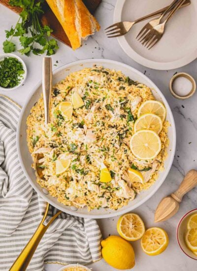 Lemon chicken orzo in a skillet with lemons, bread, and plates in the background.