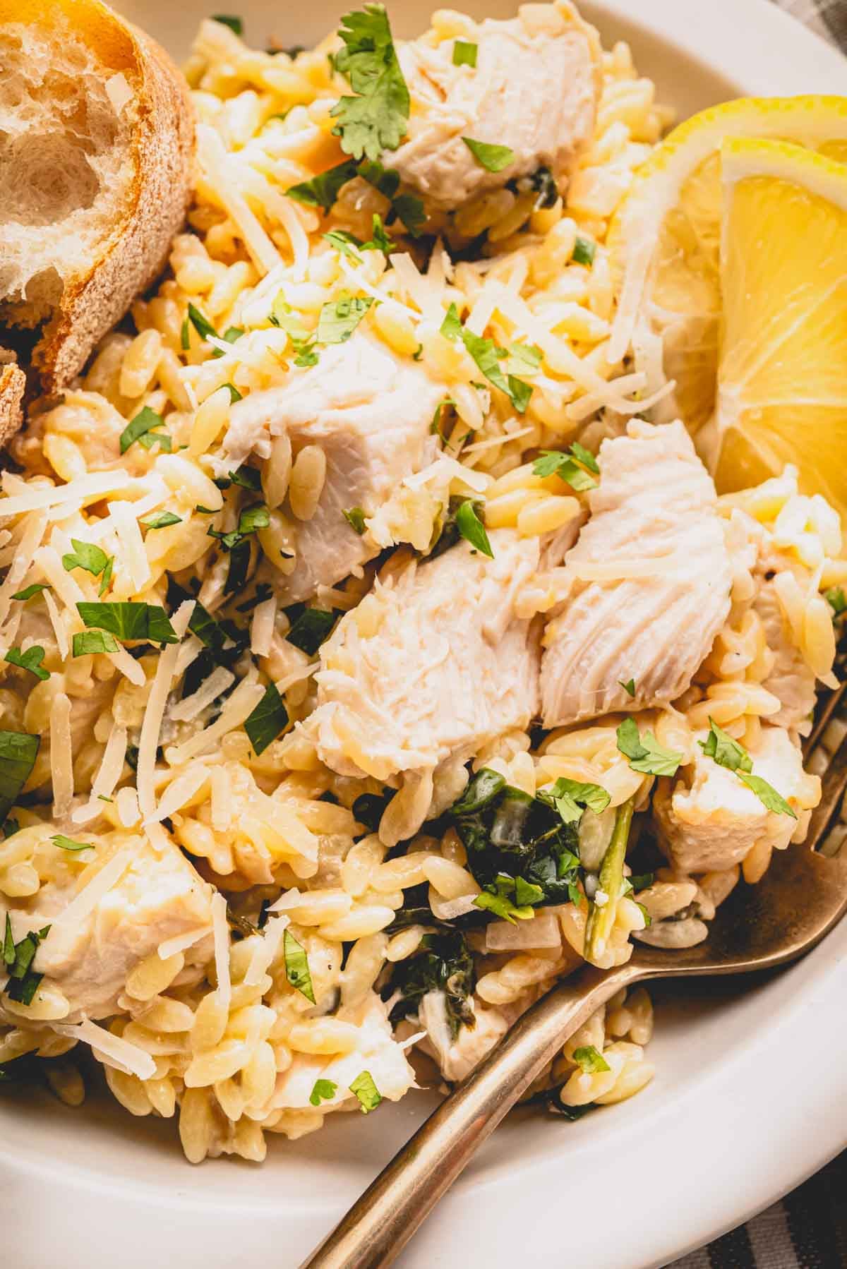 Close up image of lemon chicken orzo in a white bowl with a fork.
