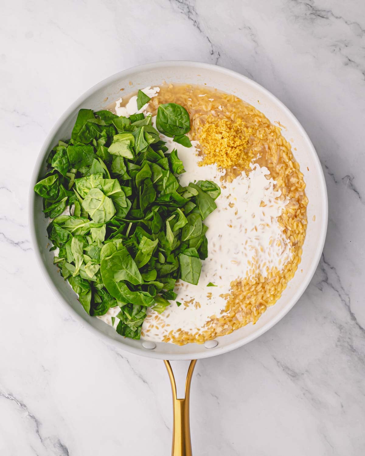 A white skillet with orzo, cream, and baby spinach.